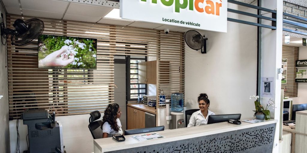 Photographie d'un comptoir de location de voiture à l'aéroport Roland Garros de La Réunion, montrant deux hotesses d'accueil souriantes et accueillantes prêtes à renseigner les clients